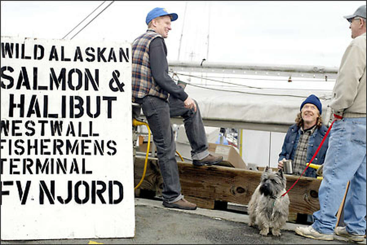 Mark Johansen, left, and Pete Knutson, center, talk with Mark's father, Gary Johansen, shown with his dog, Bart, at the West Wall at Fishermen's Terminal. The fishermen are selling salmon, halibut and prawns to the public, which they caught and froze at sea off Alaska.