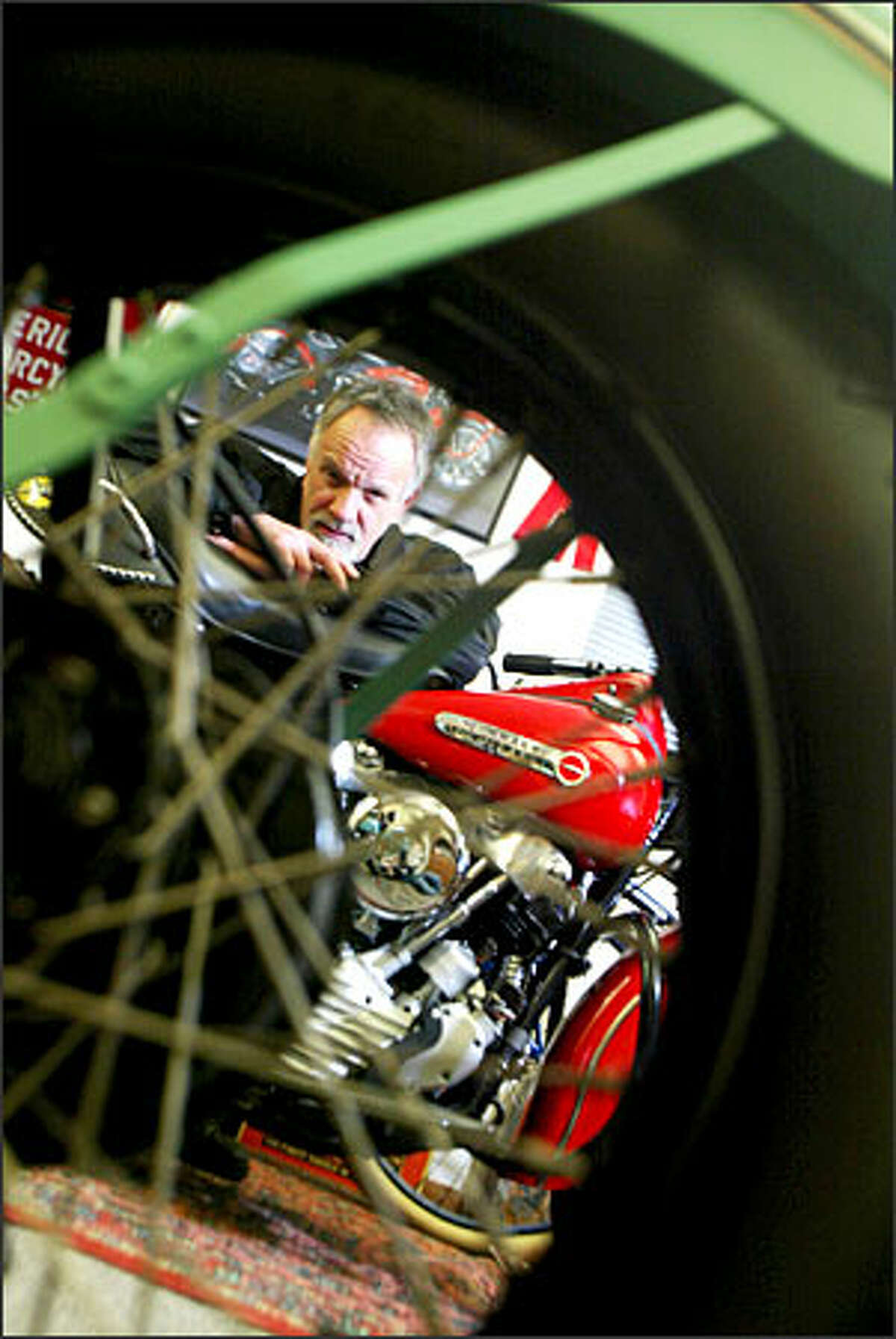 Marty Maloney leans on a 1947 Harley Davidson "knucklehead" as he looks through the wheel of a 1938 Harley Davidson UL.