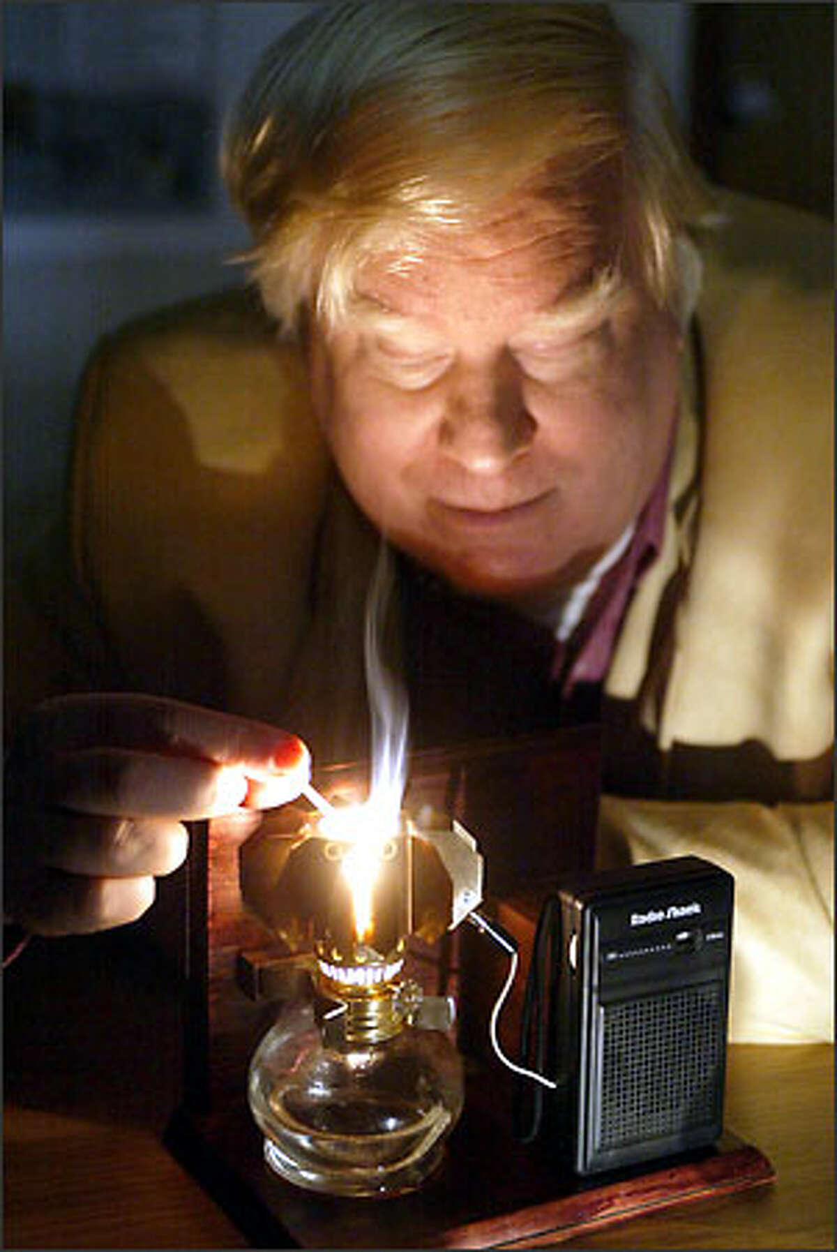 Lewis Fraas, president and CEO of JX Crystals in Issaquah, lights a Thermo PV device that holds lamp oil, and by lighting the oil he powers the radio. It's the oil lamp shade that makes this little device special.