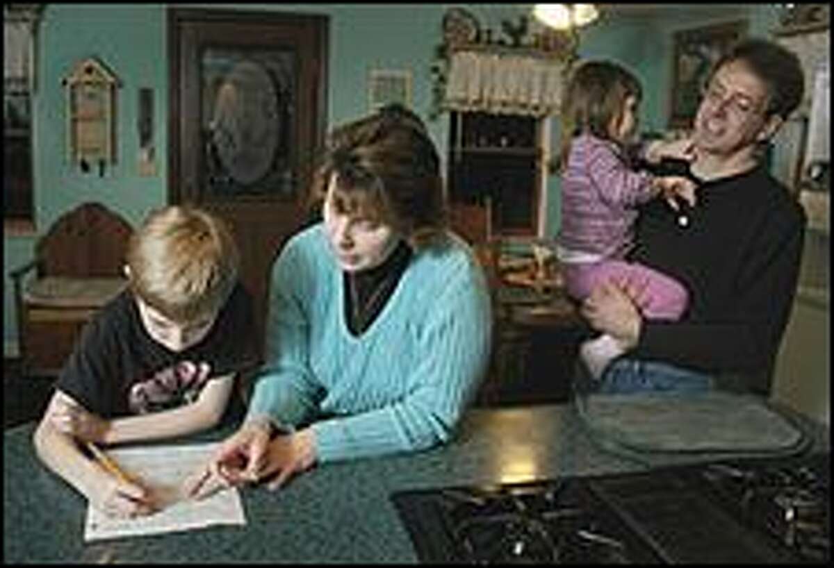 Grace Case, second left, helps her son Adam, left, with his math homework as her husband, Dan, right, and daughter Emily look on at their home in Fulton, N.Y., on Thursday. The Cases, who accumulated over $40,000 in credit card debt, now live a frugal lifestyle in an effort to pay down the debt.