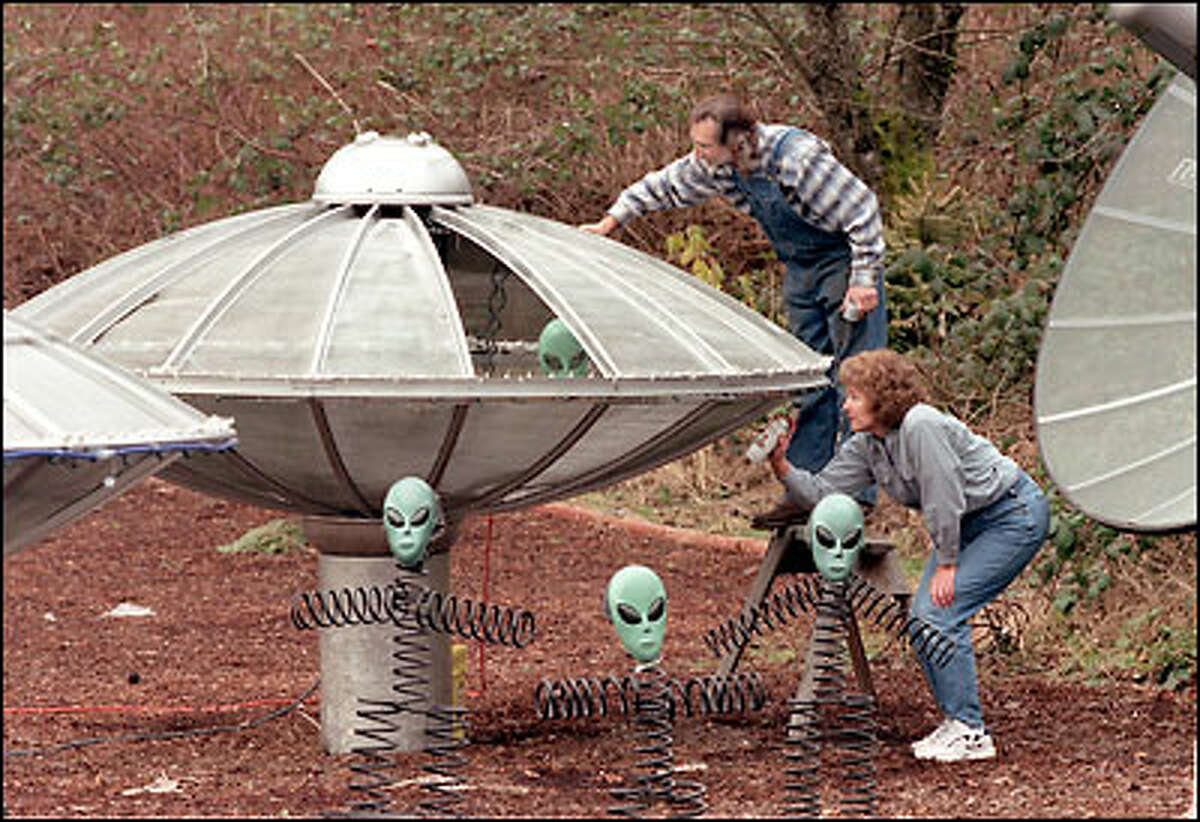 John and Sue King do a little work on the UFO display in their front yard at 20528 State Route 9 S.E. (between Clearview and Woodinville). John said he thought he'd put something up to entertain all the commuters caught in heavy traffic. John King said that one day he was getting his mail from the mail box, and a man yelled out of his car window, "I love those flying saucers." John King is handy with a welding torch and made the UFOs out of television satellite dishes and the aliens out of vehicle springs and Halloween masks. The Kings have even added Christmas lights and a sound system. Every once in a while they have to use cords tied to tires to keep the ships from "flying" during gusty storms. The project has turned out to be a lot of fun. "I've enjoyed giving something to the commuters," he said.