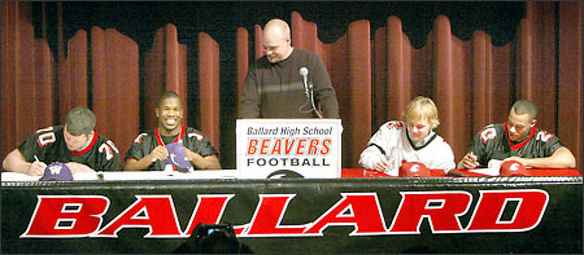 Ballard High School football coach Doug Trainor, center, savors the moment as four of his players sign national letters of intent to play for Division I rivals Washington and Washington State. From left, lineman Tyler Ashby and safety Keauntea Bankhead signed with the UW, while quarterback Cole Morgan and running back J.T. Diederichs signed with WSU.