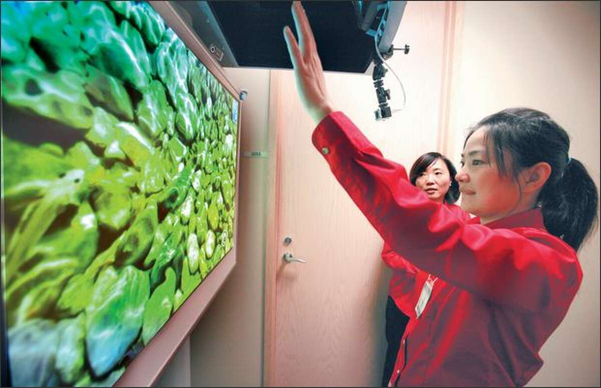 Heng Zhang, project manager in Microsoft's adCenter Labs, demonstrates Air Wave, an interactive display, Tuesday, as Li Li, the lab's group manager, watches.