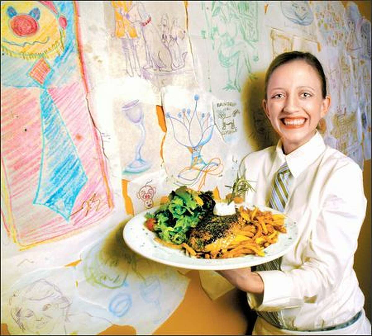 Standing next to a wall of customers' crayon art, Rachel Dreyer, a server at XO Bistro, holds a plate of steak frites with steak, salad and fries.
