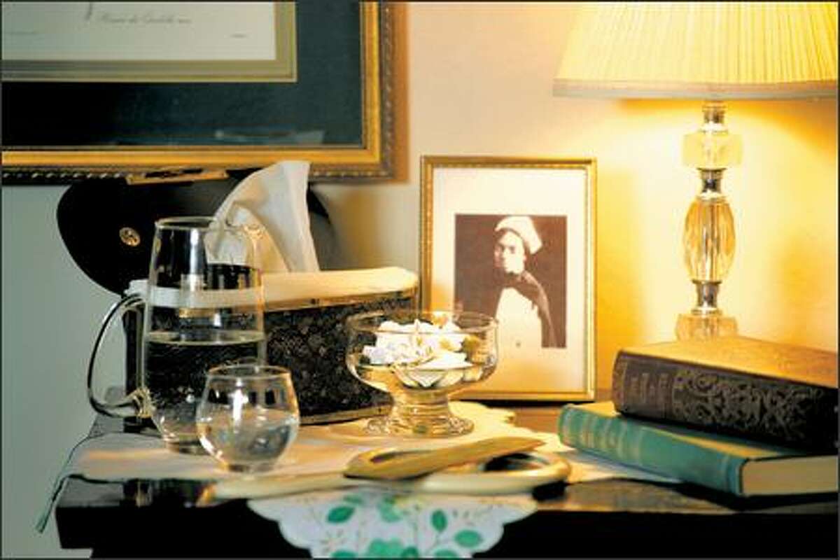 A bedside table from Goodwill with a vintage picture frame and books is illuminated by a faux cut-crystal lamp. A Lucite-style woman's purse creatively hides the tissue box.