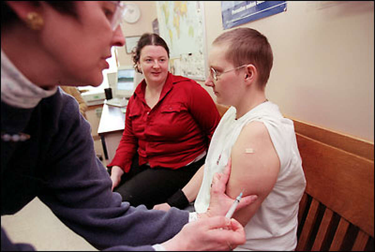 Marlys Seeman, immunization nurse at the King County's Belltown Public Health Center, administers a measles immunization to Salem and Jennifer St. Pierre.
