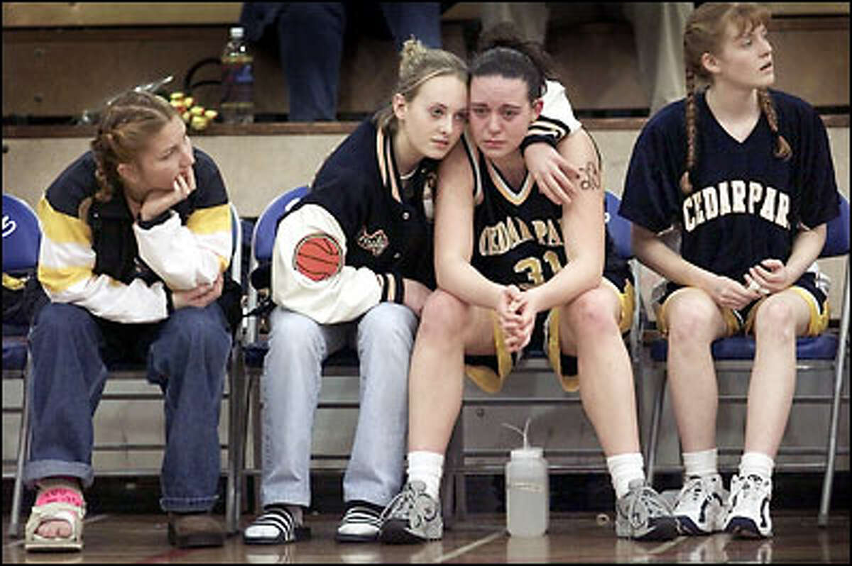 Cedar Park Christian High School's Emily Harrison comforts her tearful teammate, Mandy Janes, last night as their chance to advance in the girls Class B state tournament is ended by Shoreline Christian High School. Injured senior Julie Kirkland, left, and player Stacie Swicord, right, watch the game in Seattle's Ingraham High School gymnasium.