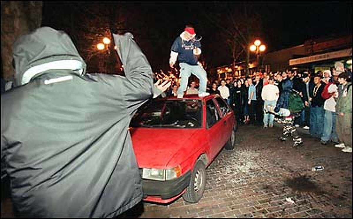 While a large crowd watches, a man jumps on top of a parked car that was seriously damaged when Mardi Gras celebrations in Pioneer Square degenerated into a riot early this morning.