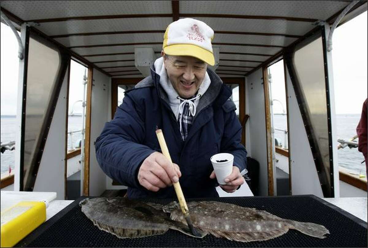 Masaro Tahara, former president of the Tengu Club, paints a flounder with ink Sunday before putting paper over it to make a print while fishing near Hansville.