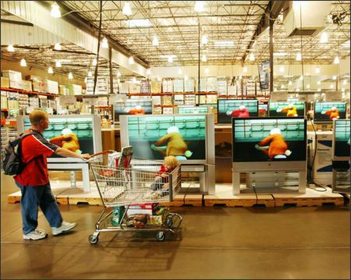 Paul Gibbons and his daughter Anna parade past big-screen TVs at the Issaquah Costco store. Architecture critic Lawrence Cheek believes the design of such big-box retail stores imparts feelings of anonymity and alienation.