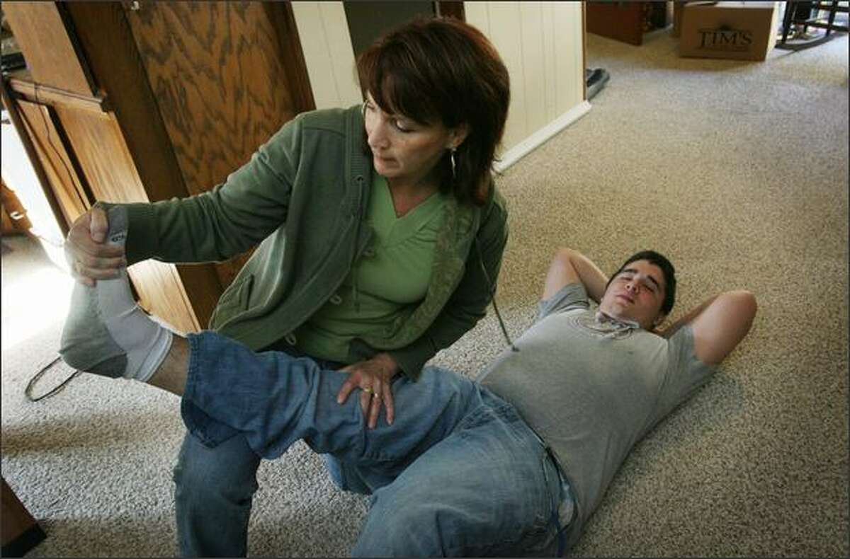 Jennifer Green stretches her son Joe's leg and Achilles' heel during a therapy session Friday in their Shoreline home. Joe was hit by a car in 2005 and suffers from a traumatic brain injury.