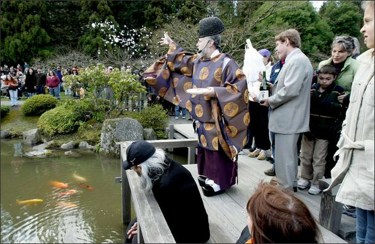 A crowd watches as the Rev. Koichi Barrish, of the Tsubaki Shinto Shrine, tosses a mixture of salt, rice, paper and sacred sand to purify the grounds of the Seattle Japanese Garden at the Arboretum during a blessing ceremony.