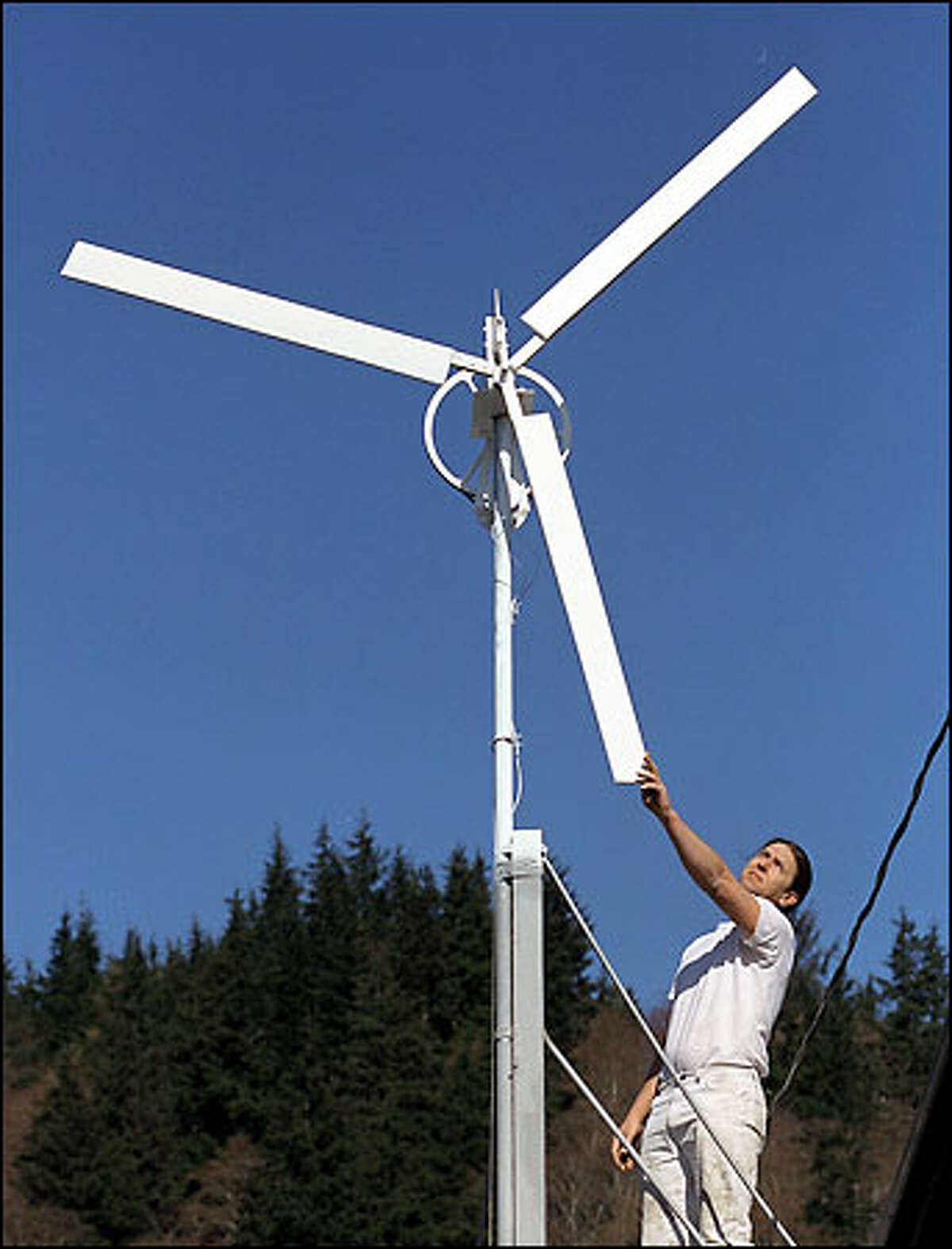 Raymond Bronk adjusts one of the four windmills that stand on his roof in Hoquiam and harness the breezes off Grays Harbor to produce electricity. More homeowners in Washington state are joining Bronk in small-scale efforts to reduce dependence on the energy grid.