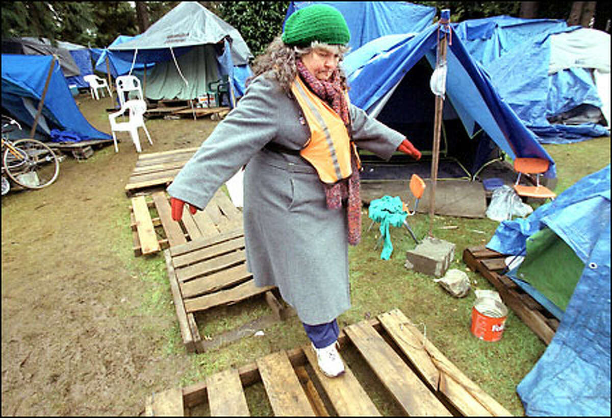 Pam Packard keeps her balance while stepping over some wooden planks to avoid the mud as she walks security at Tent City in North Seattle.