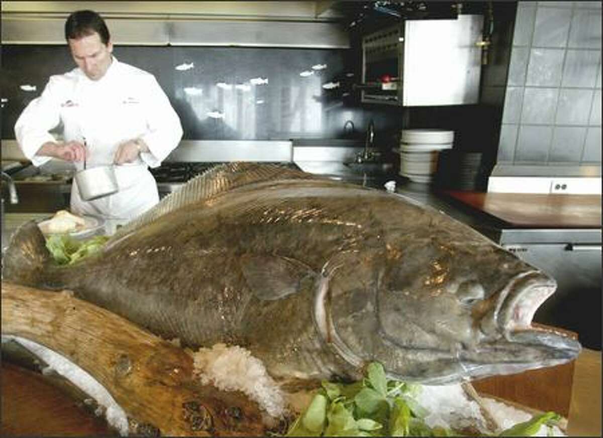 Chef Pat Donahue prepares an order of alder planked halibut behind a display of a 55-pound halibut at Anthony's Pier 66.