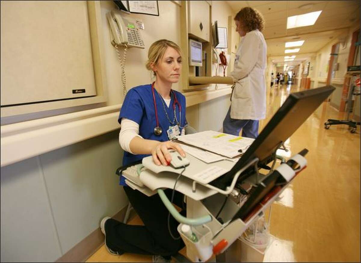 Nurse Kellie Meserve works at a wheeled workstation as physical therapist Laurie Hettinga works at a drop-down computer workstation last week at the acute care of the elderly unit in Virgina Mason Medical. The workstations are an element of Virginia Mason's effort to boost efficiency and reduce waste.