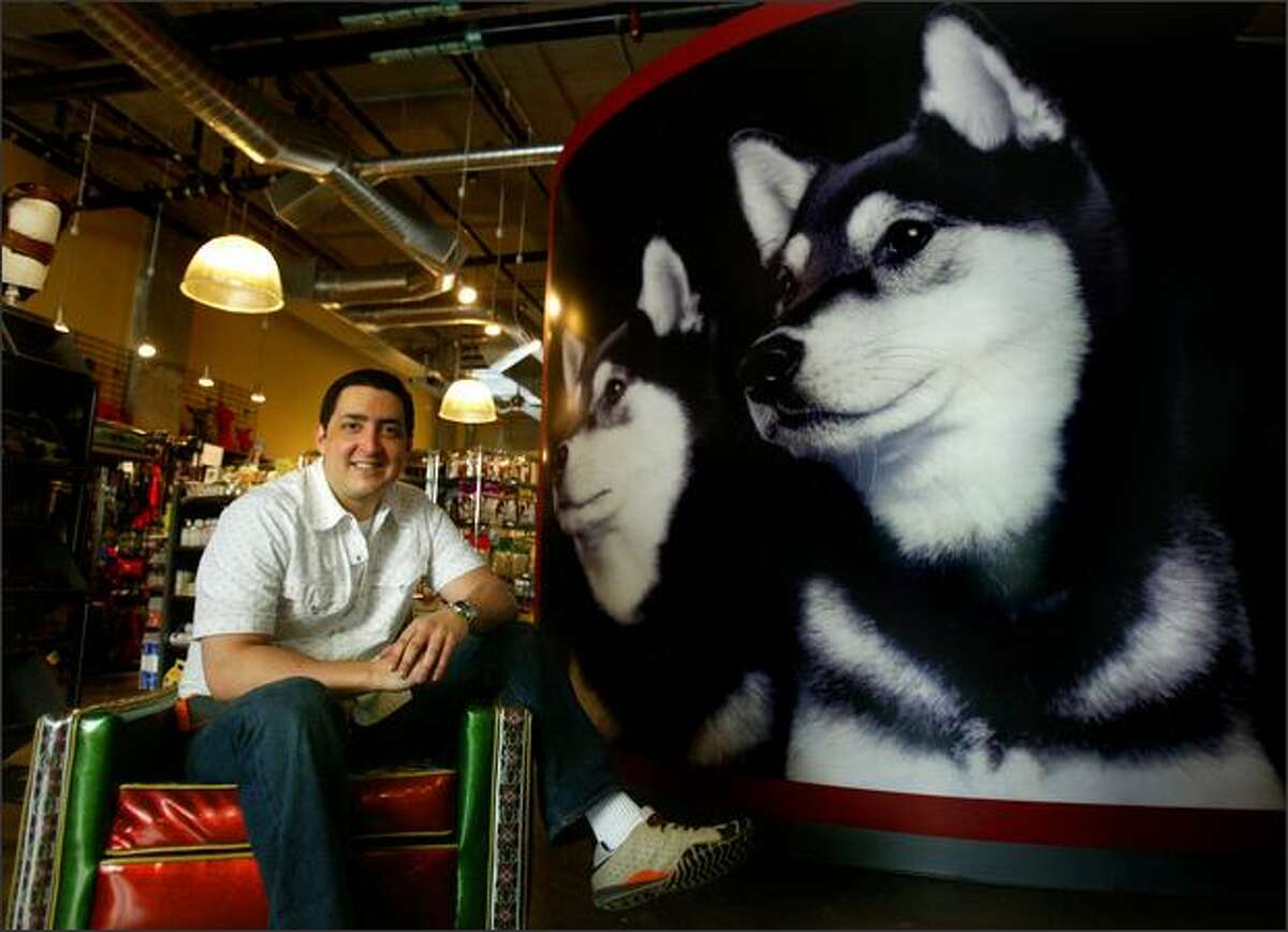 Dave Figueroa, co-owner of Scraps, an upscale boutique for dogs, sits beside a mural of his dogs in the store he has opened in the 2200 Westlake complex.