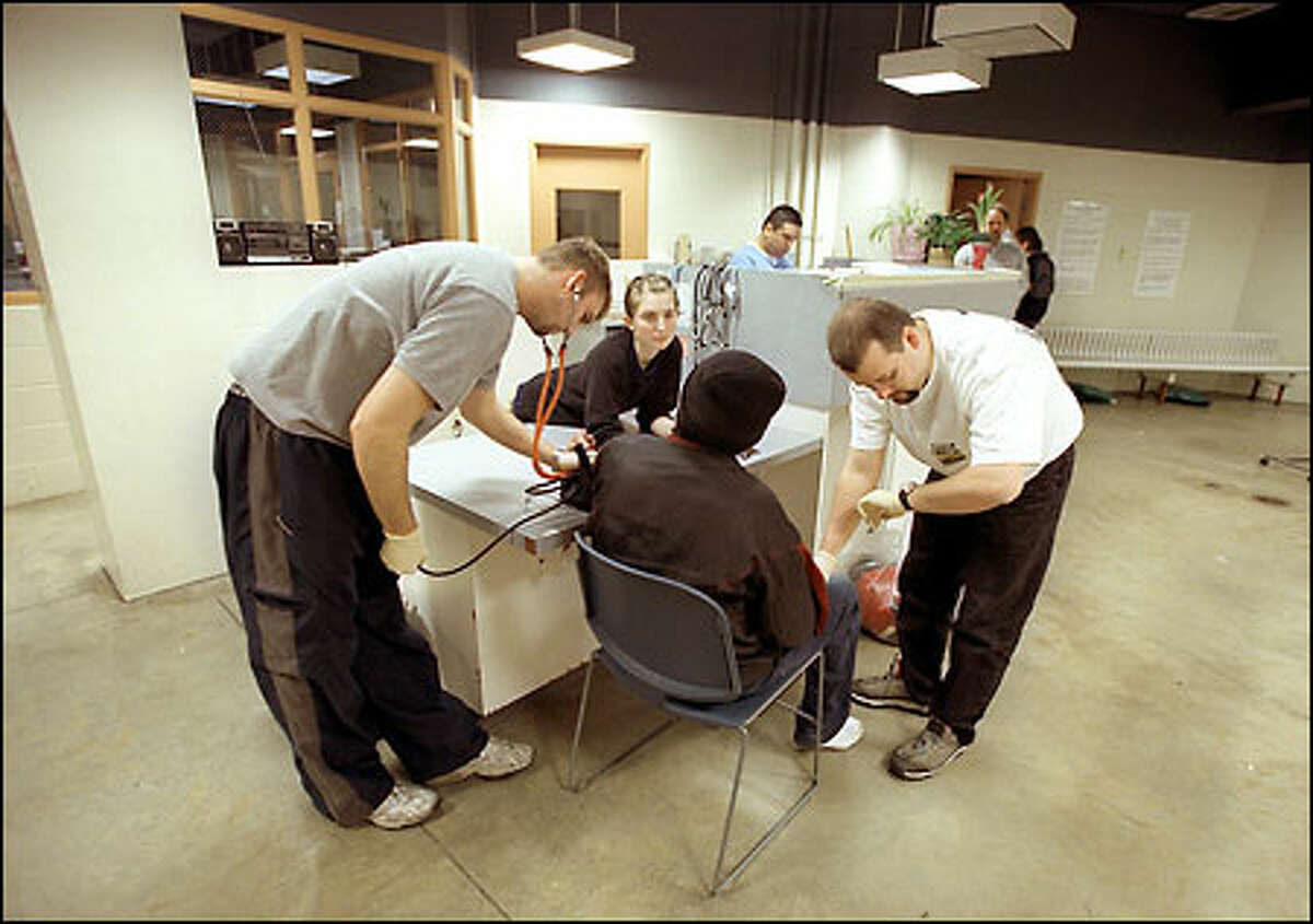 At the Dutch Shisler Sobering Support Center in Seattle, Daniel Cohen, left, Casey Aurrell, center, and Bill Craig check the vital signs of an inebriated man who walked into the center on his own.