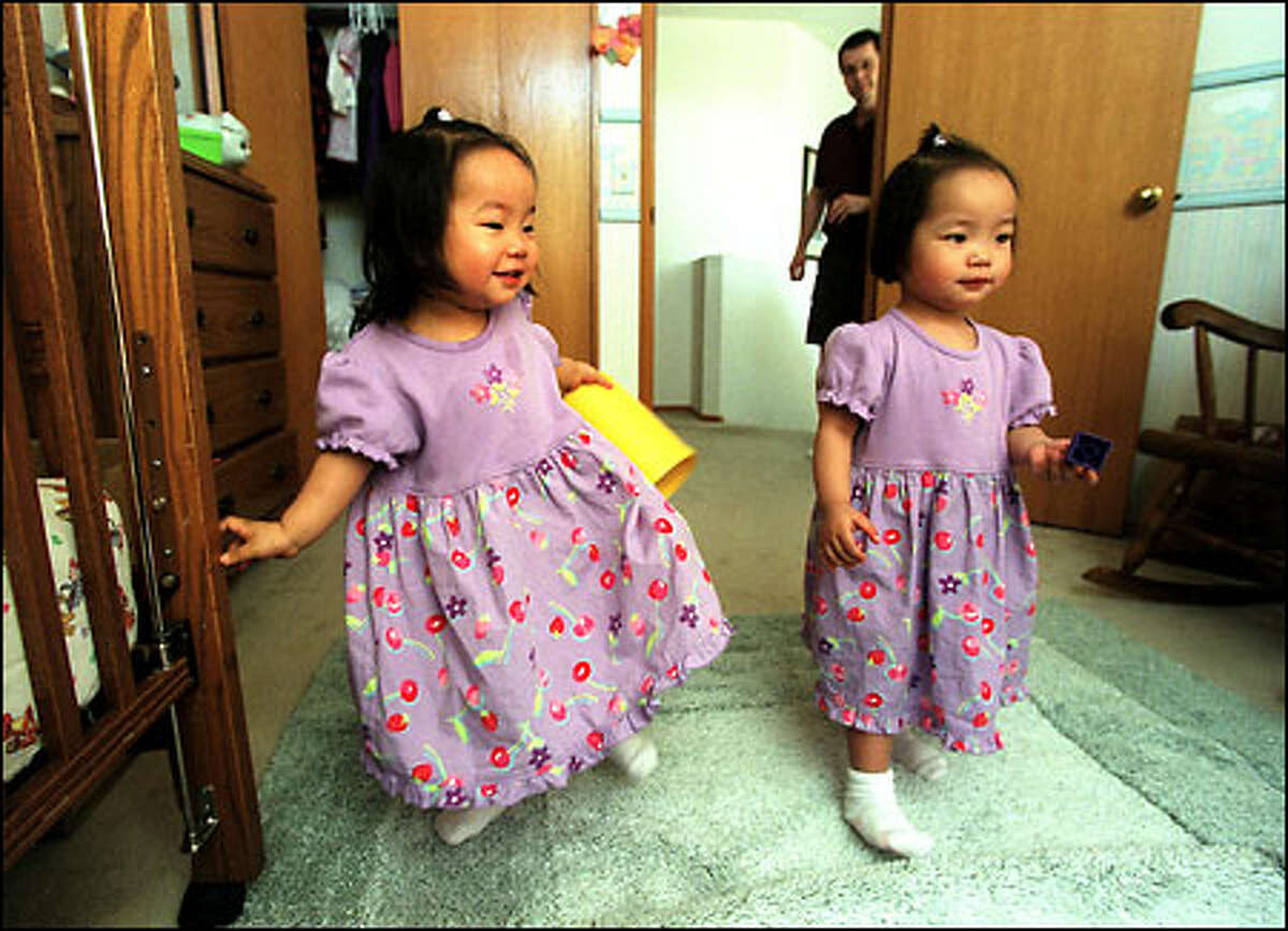 Adopted twins Cyanna, left, and Bryanna Roseen are reunited in their home in Kent. Dad Randy Roseen is in the background.