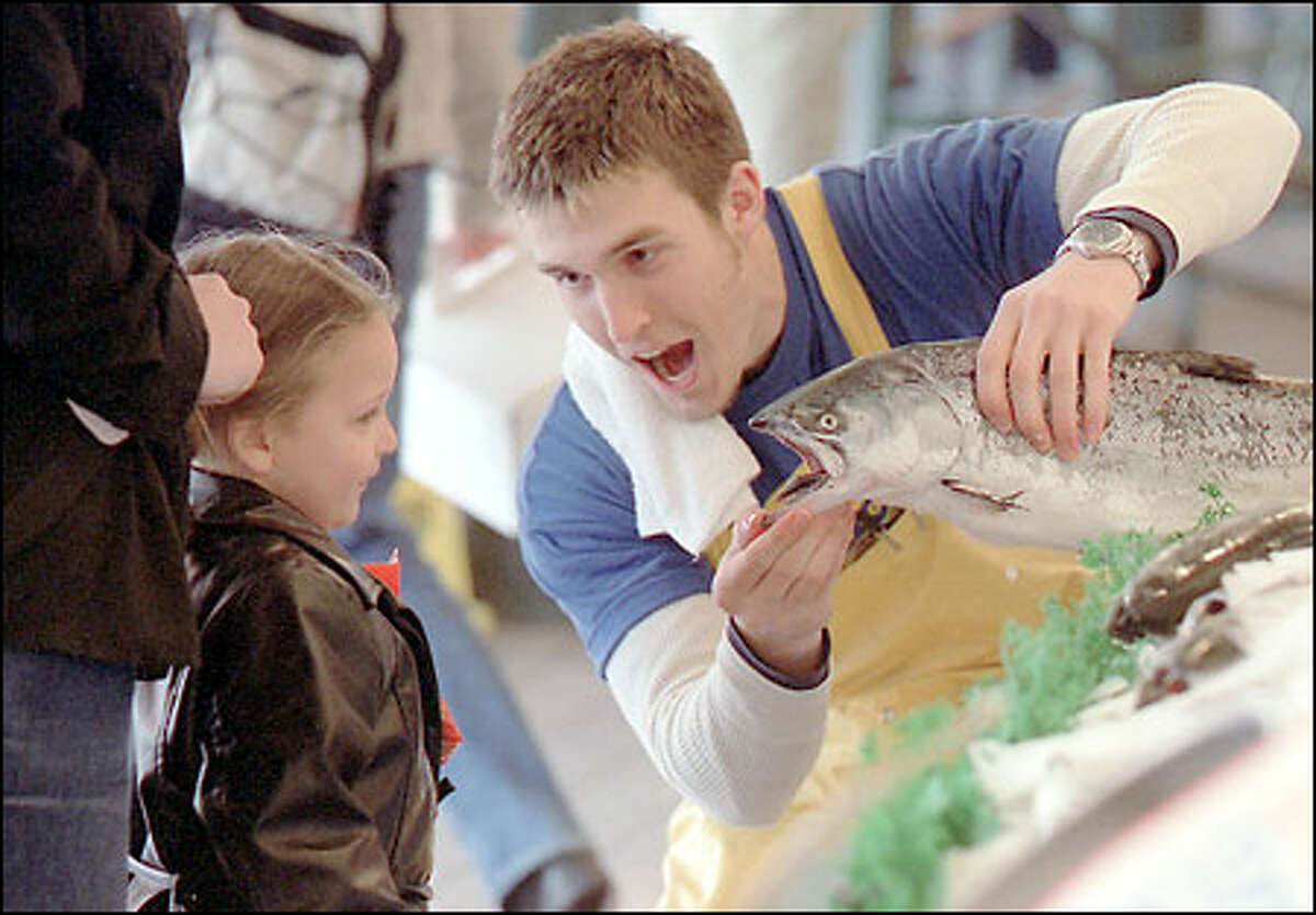 Tom Sackville-West of City Fish in the Pike Market shows Jasmine Erazo, 3, a salmon close up in the sort of good humor that has become one for the book.
