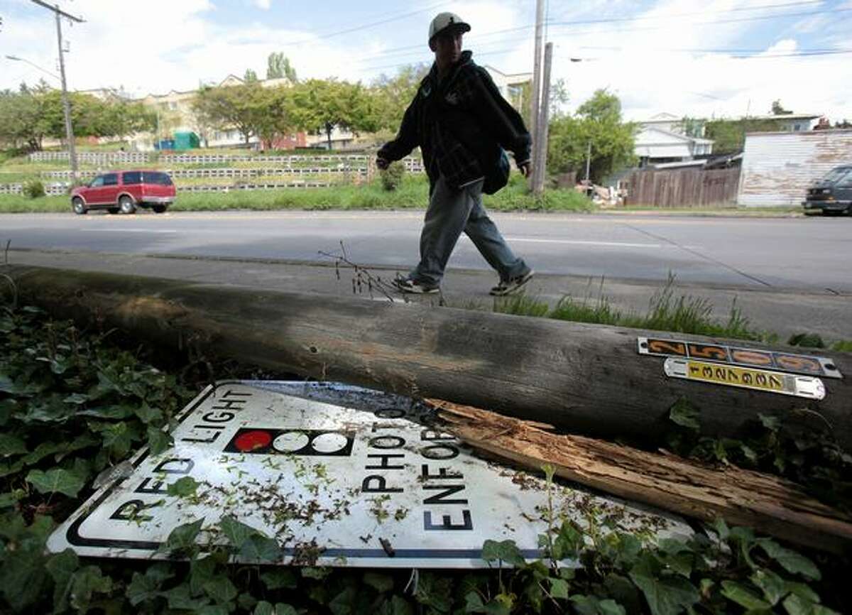 A pedestrian on Thursday walks past the remains of a red-light camera system after a car knocked down the pole that supported it at Martin Luther King Jr. Way South and South McClellan Street in Seattle.