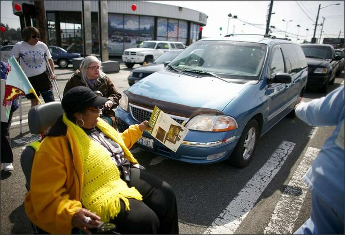 A car continues to roll into the crosswalk, bumping a marcher as Brandy Sebron-Kelley, in yellow, and other members of nearby senior citizens' residential buildings protest in the crosswalks at the intersection of Aurora Avenue North and North 130th Street. Sebron-Kelley was previously hit by a car at North 130th Street and Linden Avenue North.