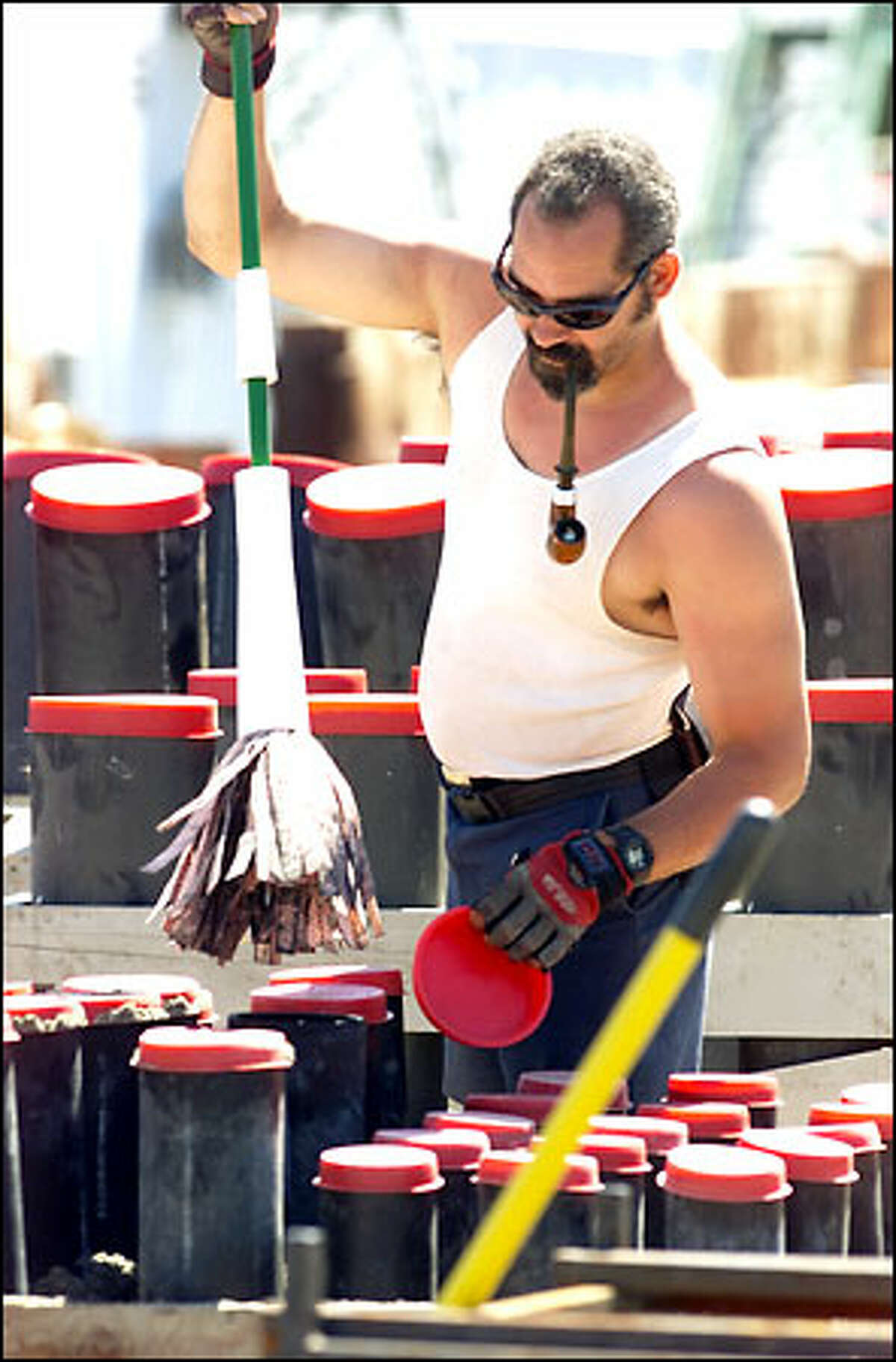 Pyro crew member Damon Gayden continues his own "irreverent tradition" of smoking a pipe while clearing mortar tubes of debris during preparations for the AT&T Family Fourth at Lake Union. At first glance the practice looks incredibly dangerous but, "Don’t worry," Gayden says. The actual fireworks are not even within the city limits yet and won’t be until mid-day of the Fourth. Until then he will enjoy his pipe at work.