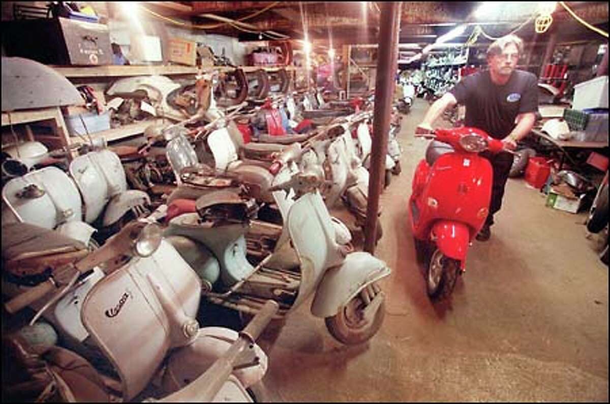 Big People Scooters salesman Steve Calvo wheels a brand spanking new Vespa past his boss' collection of old scooters. The new Vespas run from $3,000 to $4,000.