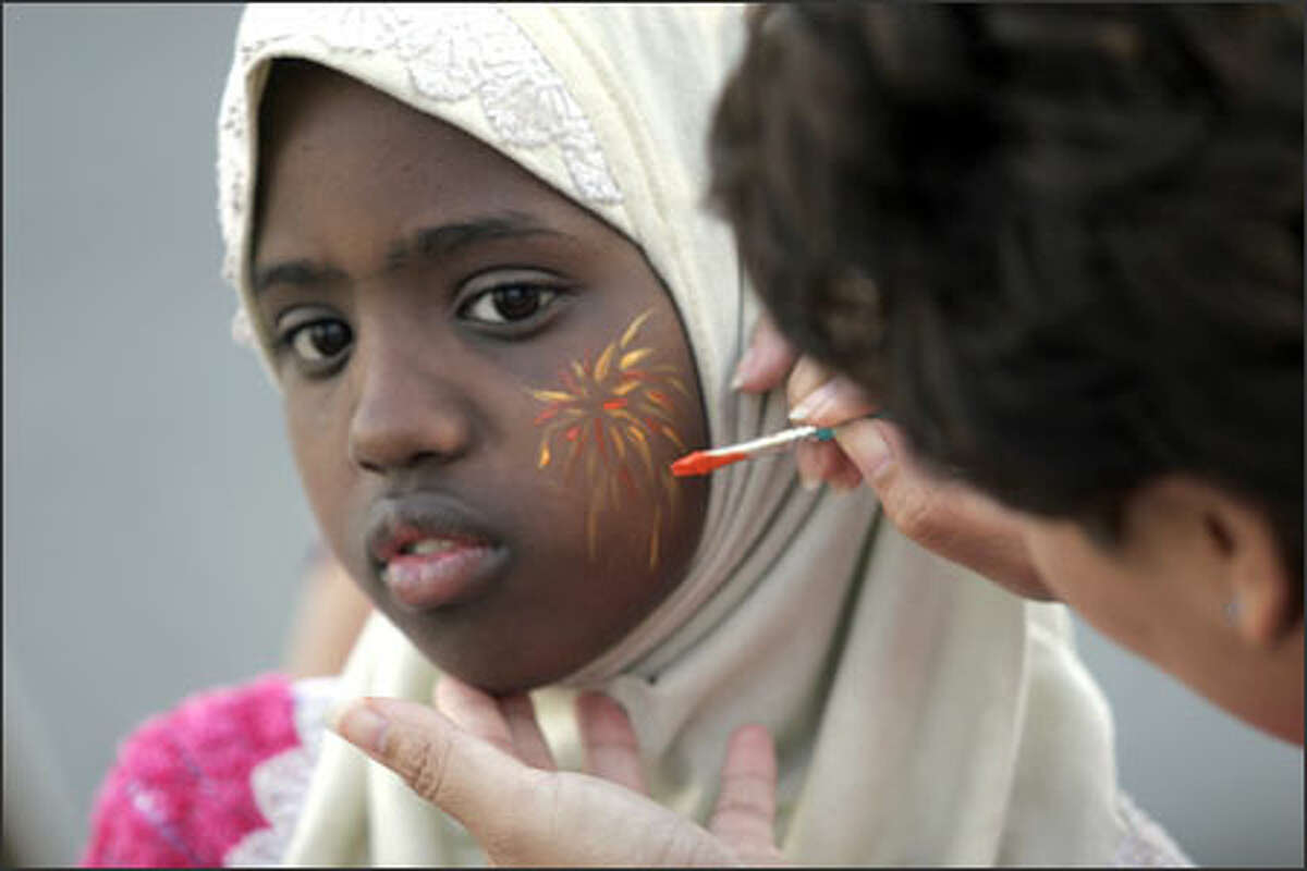 Thavy Pen, who works for the Yesler Community Center, paints fireworks on the cheek of Faduma Abdi, 12, at a neighborhood Fourth of July celebration. Last year's bad experience prompted residents of Hilltop House Retirement Residence and other groups to organize a positive festival this year.