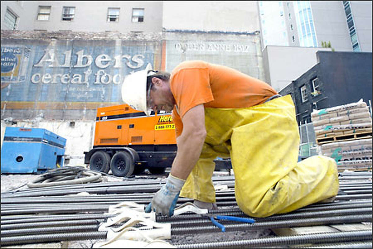 Terry Ochsner from Malcolm Drilling works on threaded nails yesterday before they are placed in the old walls of the Bethel Temple on Second Avenue in Seattle. Condominiums will be built on the site, replacing the church. The Albers cereal advertisement on the north side of the Commodore Hotel will not be covered until spring 2004 after construction of the condo building.