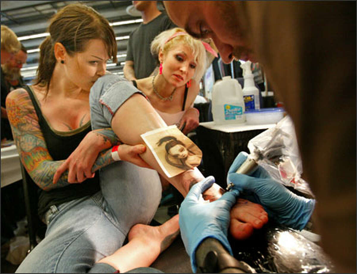 Deandra Vaughn, left, and Gisella Haladin of Vancouver, B.C., watch as tattoo artist Vic Black, from Salt Lake City, Utah, inks an image of a Mark Ryden painting onto Vaughn's foot. Vaughn made a special trip to the Seattle Tattoo Convention to see Black, who created the tattoos on her other foot and right arm.