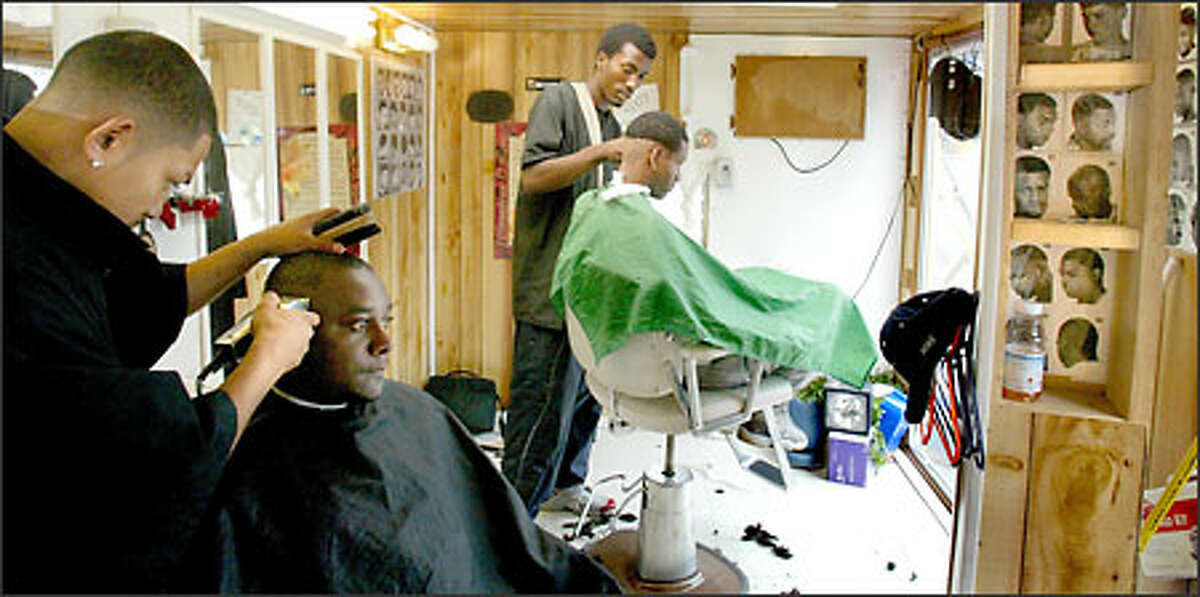 Toby Hing, left, and Arthur Dunlop, center, offer $3.99 haircuts. Dunlop plans to open another haircutting trailer, as well as a “high-class booth selling lobsters, shrimps, New Yorker steaks, T-bone steaks, fried chicken.”