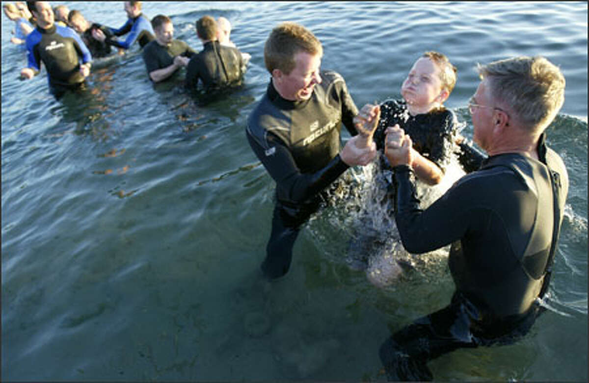 Mars Hill pastor Steve Tompkins, left, with the help of pastor Bent Meyer, baptizes his son Sam Tompkins, 9, in the chilly water at Golden Gardens Park.