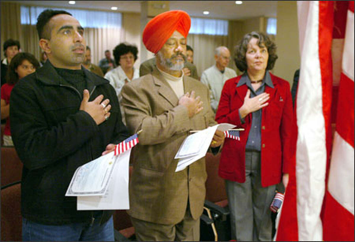 From left, Harpreet Singh, Lakhwinder Singh Bhachu and Beatriz Aramburu recite the Pledge of Allegiance during their oath of citizenship at the Department of Homeland Security yesterday in Tukwila. They registered to vote right after the ceremony in the federal office.
