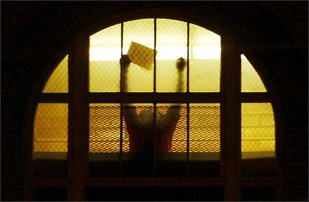 An INS detainee responds to protesters who questioned the Bush administration's special tracking registration for male visitors from mostly Muslim nations.Schenker: "It was a very rainy January night when I was assigned to photograph a candelight vigil. The crowd gathered to protest special alien registration and detention of visitors from Arab and Muslim countries. After photographing the vigil, I decided to push myself and walk with them to the INS office. When I got there I saw this detainee responding to the crowd of approximately 300 outside. I got off two frames before the INS removed him from the window."