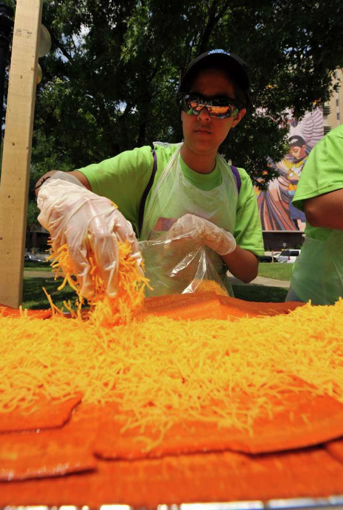 Susie Mitchell layers on some of the 1,500 pounds of Wisconsin Mild Cheddar cheese that made up the 300-foot-long enchilada made in Milam Park on April 9, 2011, as part of a collaboration between 20 local restaurants and the Rey Feo Consejo Foundation.