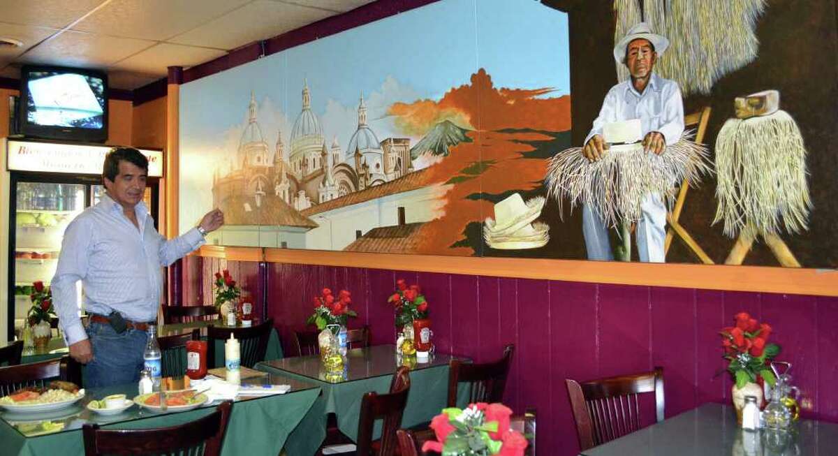 Wilson Hernandez, owner of La Mitad del Mundo restaurant in Danbury, shows a mural with the Cathedral of Cuenca, the Andes mountains, and "Panama hats." The mural hangs in his restaurant.