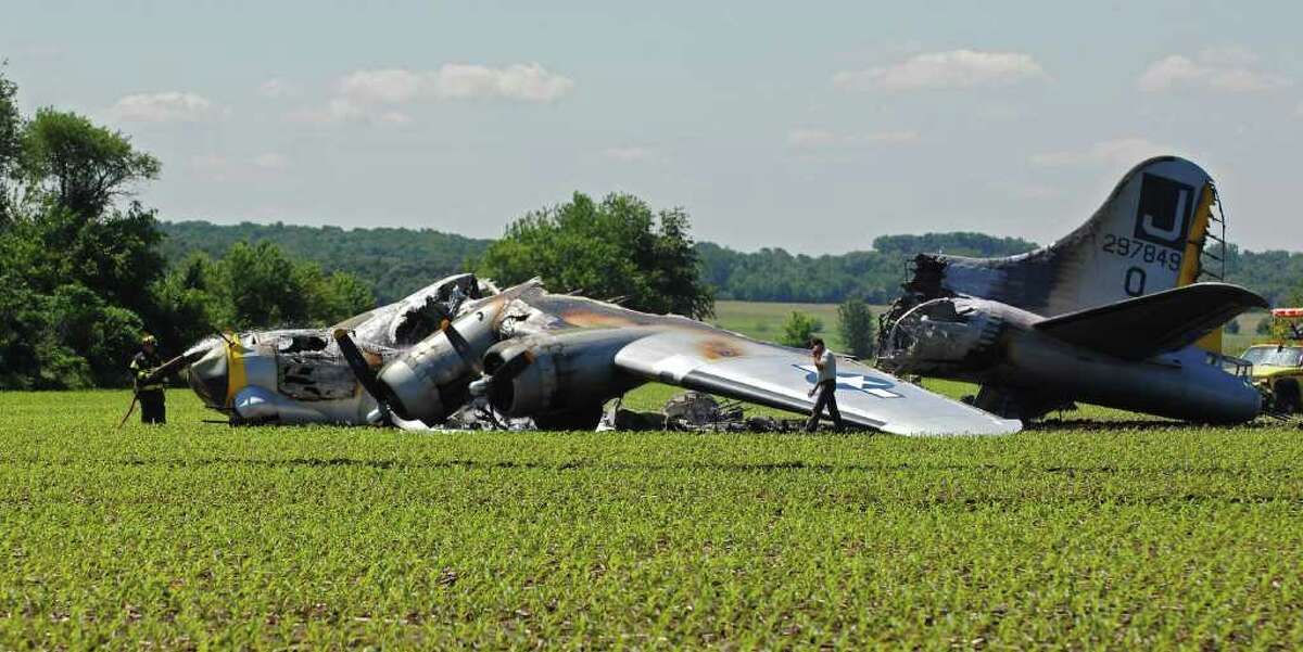 Emergency personnel are seen by the World War II-era Boeing B-17 "Liberyt Belle" after it burned following an emergency landing in a farm field in Oswego, Ill.,. Monday, June 13, 2011. The vintage plane had taken off from nearby Aurora Municipal Airport. The Federal Aviation Administration believes the seven people on board the plane escaped uninjured.