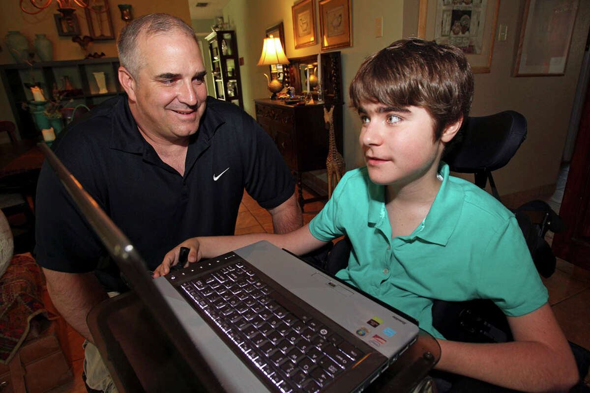 Disabled high school student Ralyn Parkhill works on his computer with help from instructional assistant David Carnes at home on June 15, 2011.