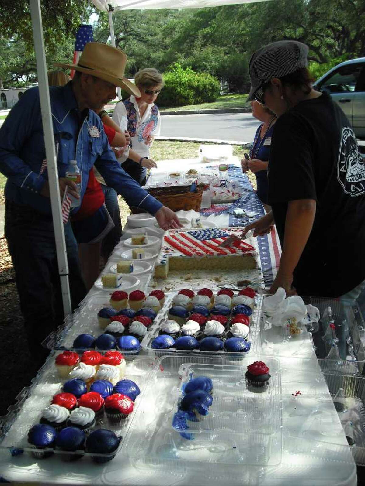 Olmos Park residents, including Mayor Susan Gragg (left background) browse patriotic treats at the city’s Fourth of July picnic Monday at Alameda Circle. The food pictured here were offered by Frankie Boone of Converse-based FrankieB Bakery & Catering (right background) and Olmos Park-based Sylvia Toscano of All Aboard Deli and Bistro (right forefront).