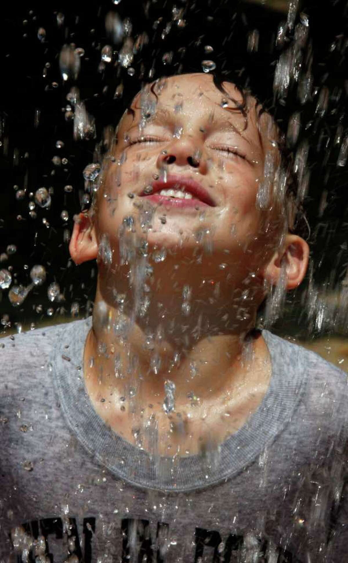 Carson Dziekan cools off playing in a water fountain during the hot summer weather at a park in Batavia, N.Y., on Monday,.