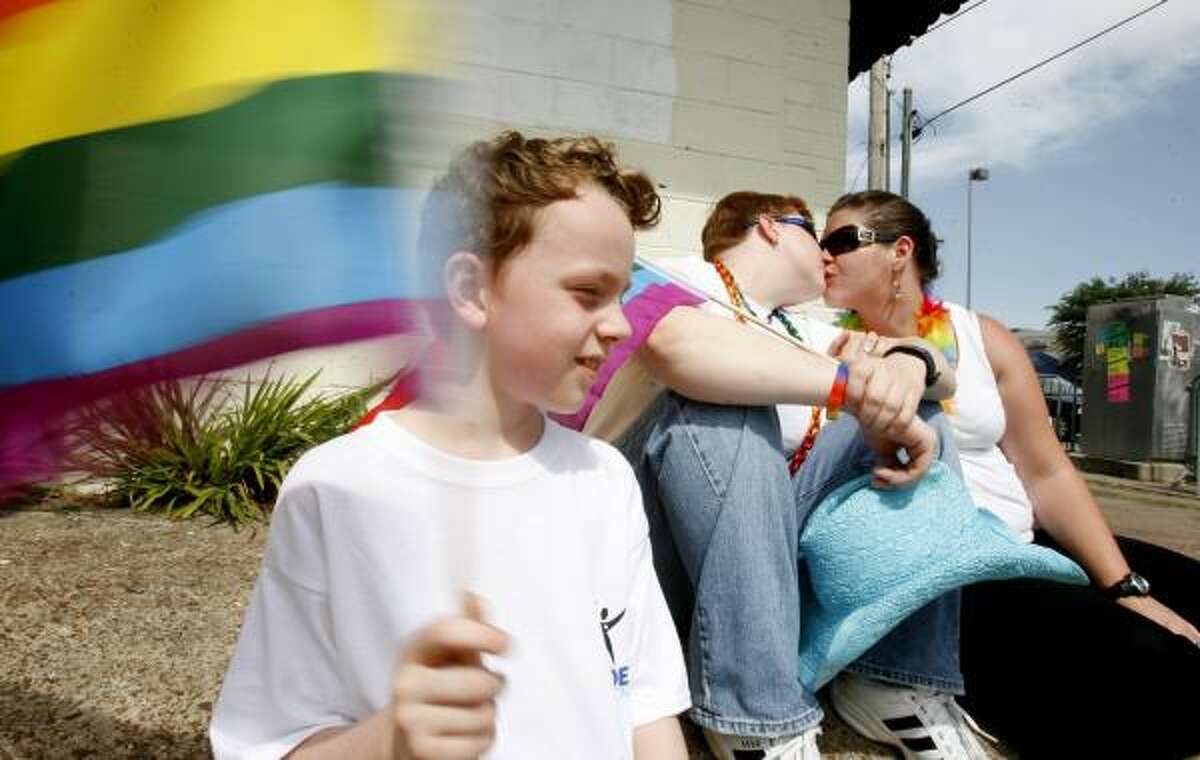 Keilan Levesque, 7, waves a flag as his mother, Reye Levesque, center, and Sarah McDurm kiss alongside Westheimer before Saturday's 30th annual Houston Pride Parade.