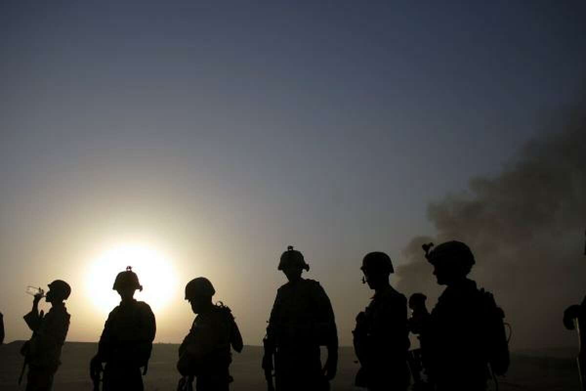 Iraqi army soldiers, accompanied by U.S. Army soldiers, walk down a field as plumes of smoke rise from a burned irrigation canal outside Balad Ruiz. The soldiers were searching for weapons caches.