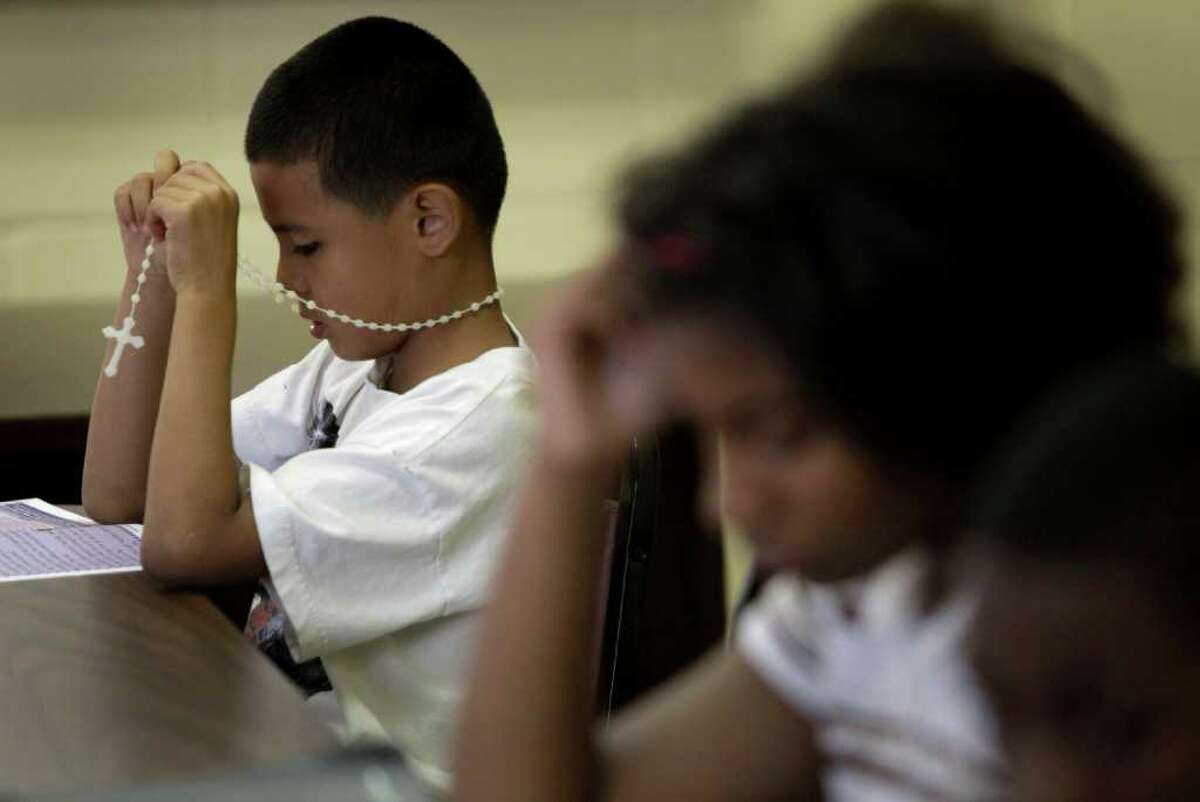 Jesus Torres, 8, left, holds his Rosary as he and classmates Deajah Kanady, 11, center, and Franciso Lizado, 12, right, read a lesson during Vacation Bible School at True Light Missionary Baptist Church, 7102 N. Main, Wednesday, July 13, 2011, in Houston. Although the church is Baptist, they are reaching out to the community and welcoming other religions to their church. Independence Heights, the first incorporated African-American city in Texas, now is almost half Latino. The church provides round trip van transportation from his apartment complex. ( Melissa Phillip / Houston Chronicle )