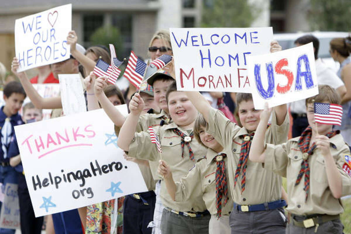 Boy Scouts hold signs and wave flags outside the new home of Retired Capt. Daniel Moran and his family as they wait for the arrival of Secretary of Defense Robert Gates.