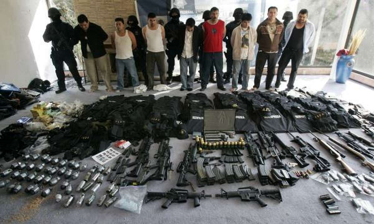 Men arrested by Mexican federal police stand behind weapons found Tuesday in a home in Mexico City.