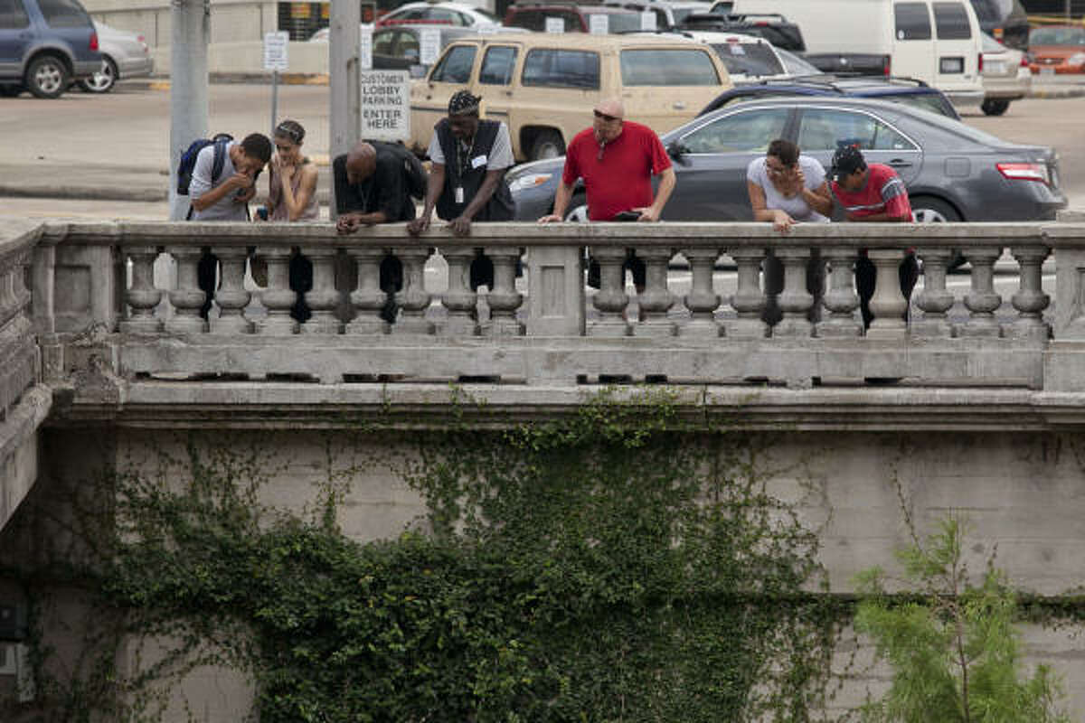 Pedestrians watch as HPD investigators examine the body recovered from Buffalo Bayou under a downtown bridge. The woman who found the body said she knew the man as "Detroit."