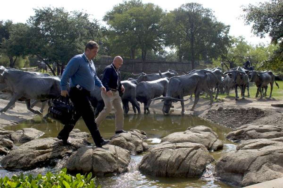 Eric Bergin of Salt Lake City and Brian Lowe of San Diego walk on rocks through Pioneer Plaza next to bronze steers while on their way to the Dallas Convention Center.