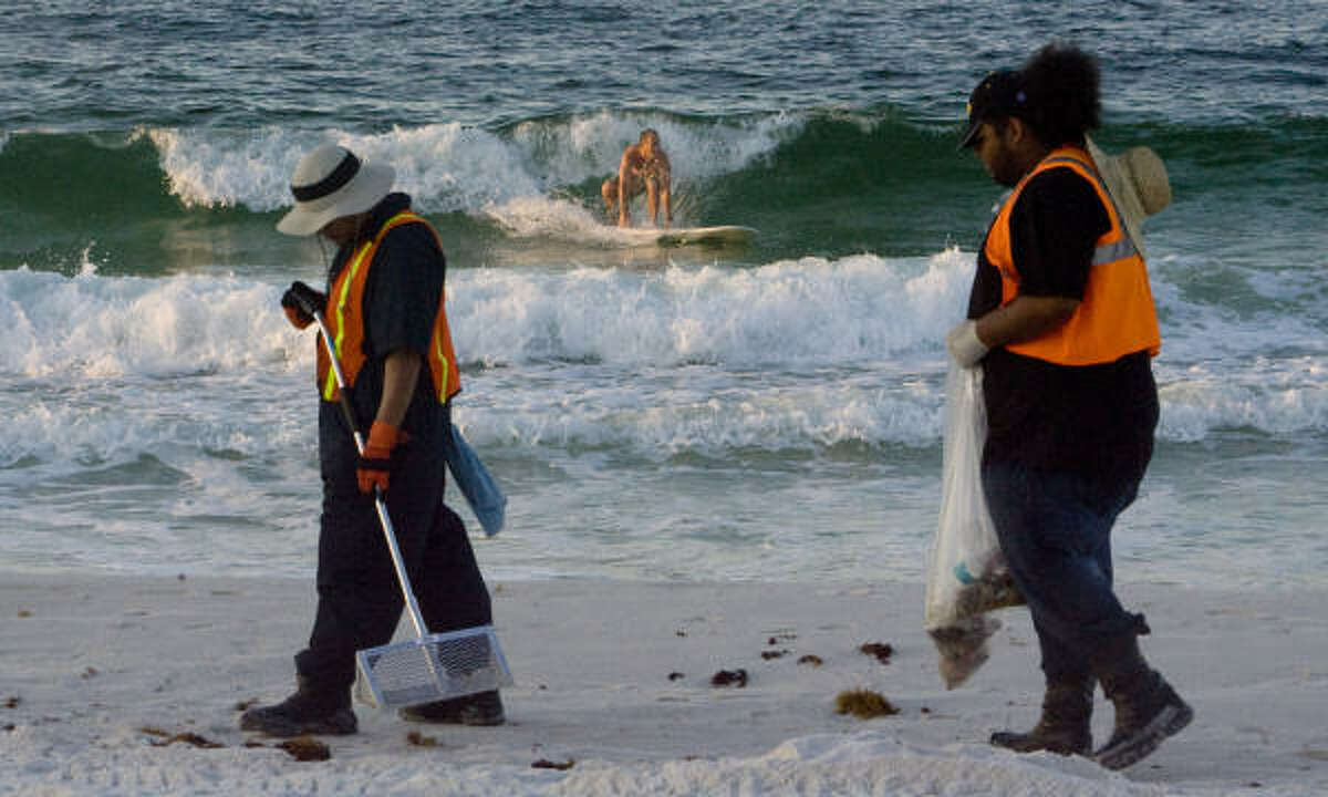 A surfer works to find a wave in the gulf as British Petroleum clean up crews walk along Pensacola Beach looking for and cleaning up small bits of oil debris from the Deepwater Horizon oil spill in Pensacola.