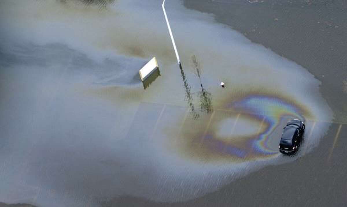 An oil slick spreads from a car in a flooded parking lot of an office complex in Cranston, R.I.